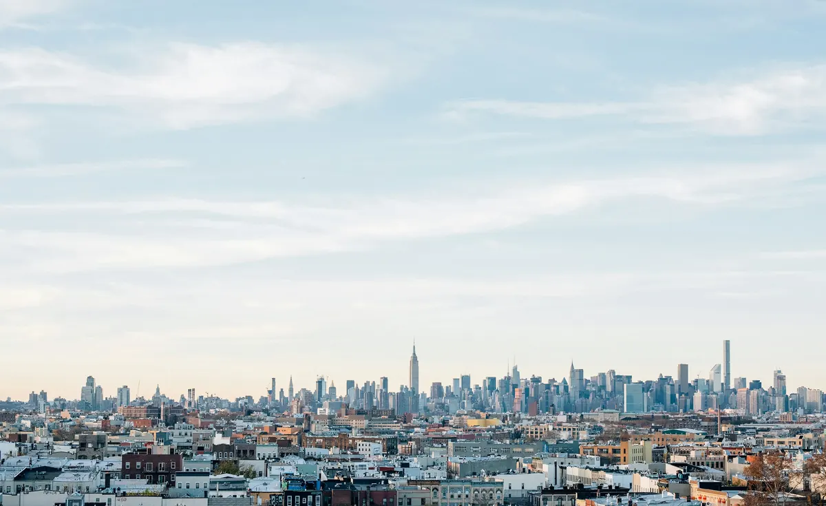 The Manhattan skyline seen over low brick rooftops under a pale morning sky