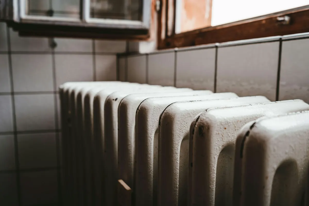 A white cast-iron radiator beneath a window, in soft side light