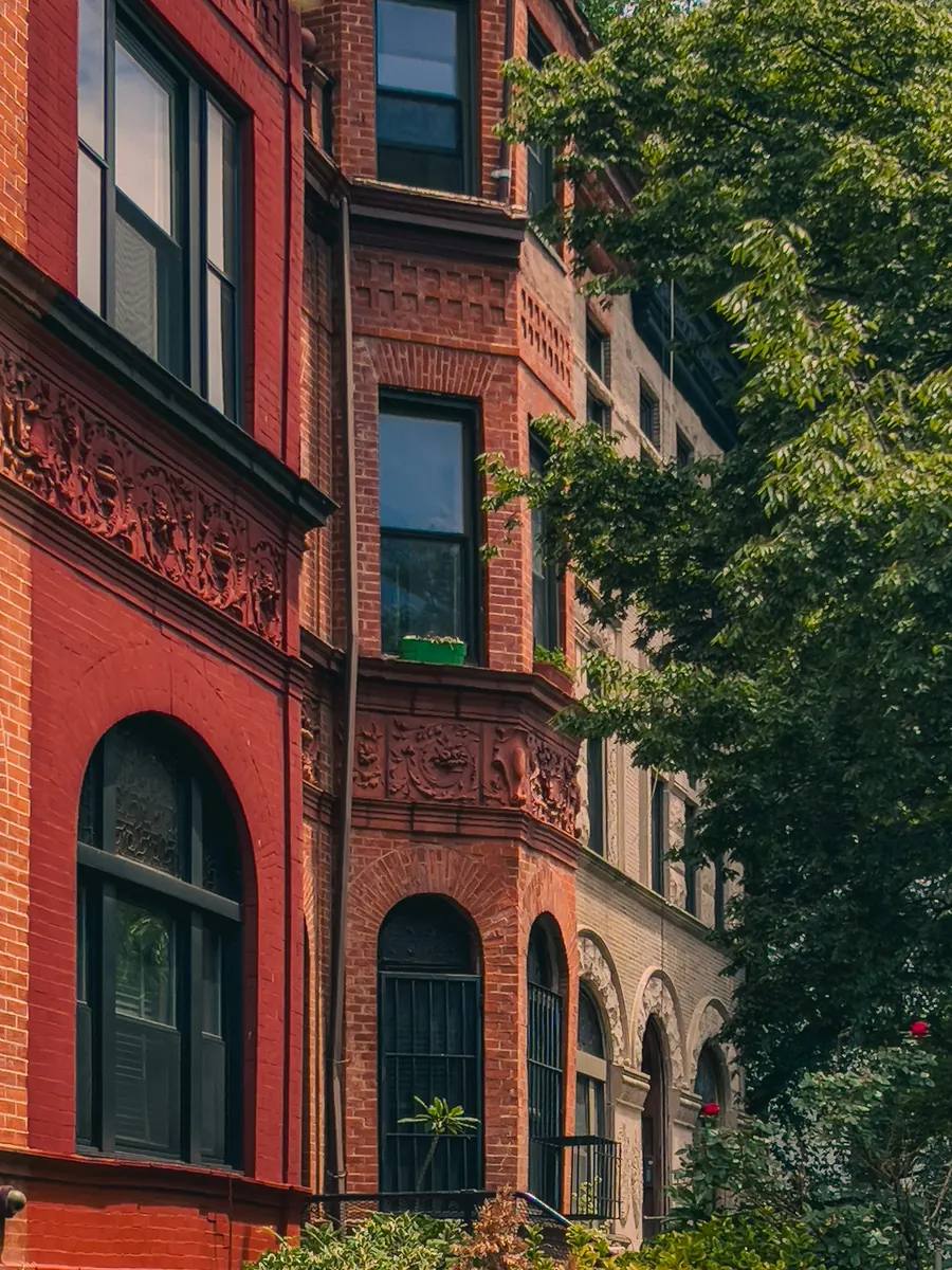 A red-brick New York building with carved terracotta panels, a bay window and arched windows beside a leafy tree
