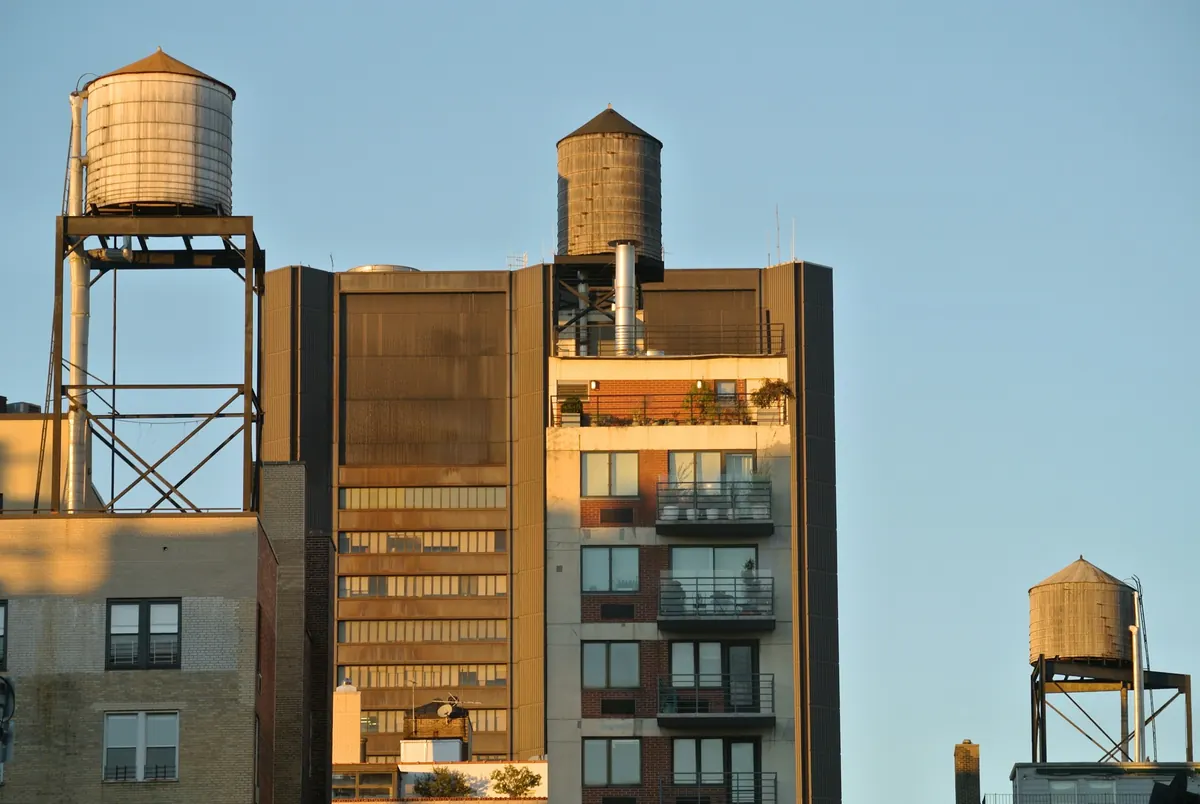 Three wooden water tanks on tall New York rooftops in warm late-afternoon light against a clear blue sky